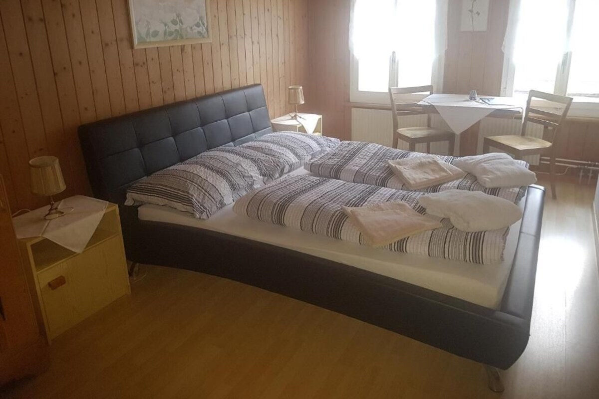 A bedroom with a bed, bedside tables, a window, and a dining area.