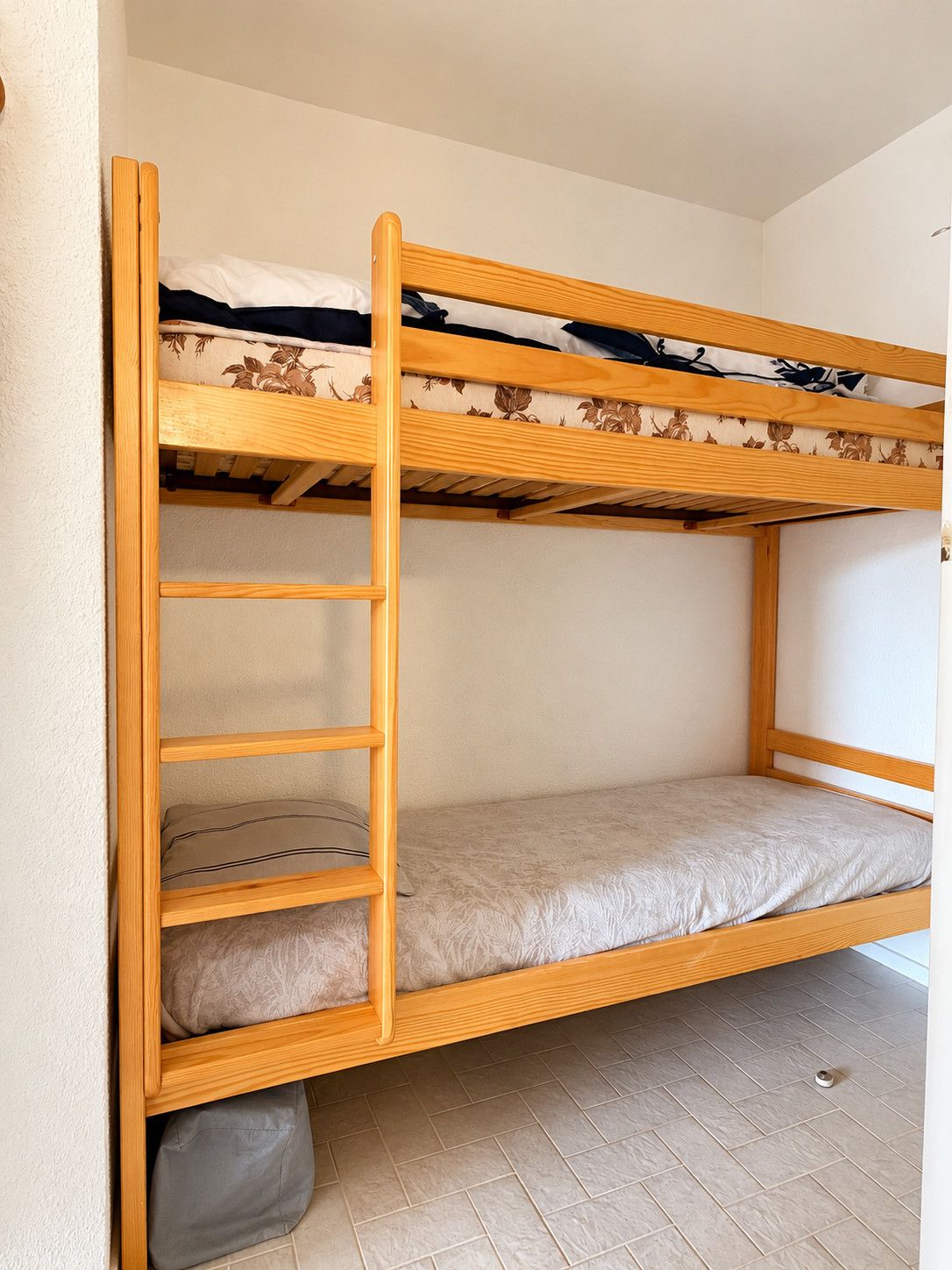 Un lit superposé avec une échelle en bois, une étagère inférieure et un matelas recouvert d’un tissu à motifs.
