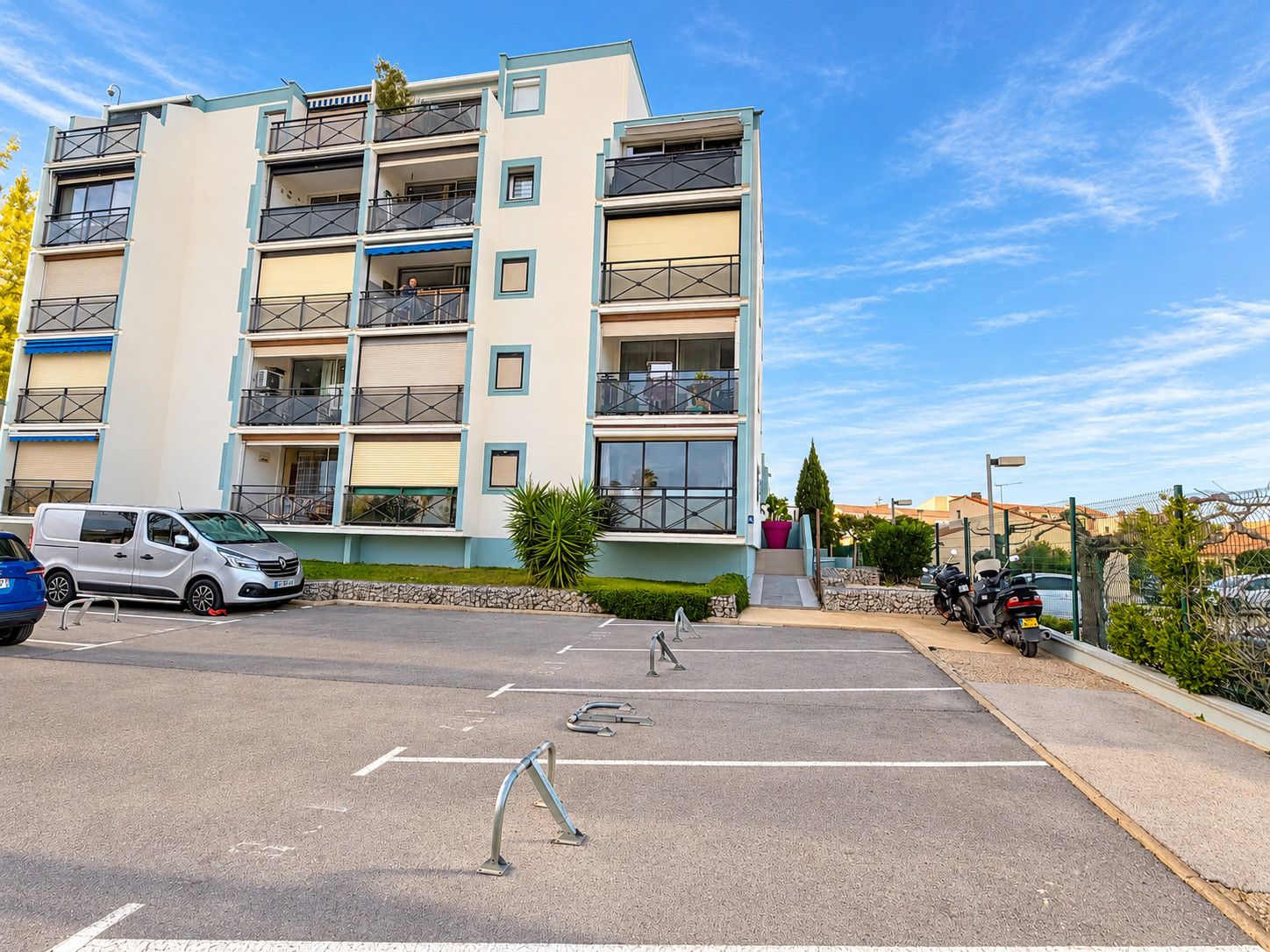 Un immeuble résidentiel à plusieurs étages, doté de balcons, d’un espace de stationnement et surplombant un ciel dégagé.