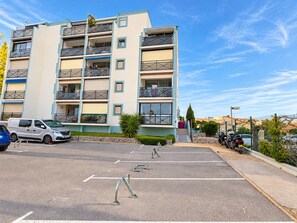 Een meerlaags woongebouw met balkons, een parkeerplaats en een heldere lucht.