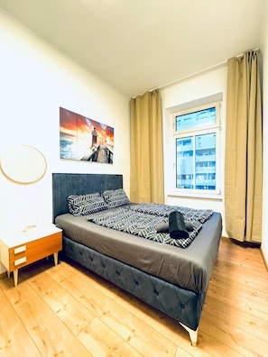 A bedroom with a bed, a nightstand, a window with curtains, and a painting on the wall. - Hello Vienna Private Room near FAC Platz (Wien)
