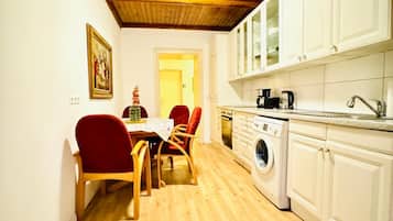 Une cuisine compacte avec des meubles blancs, un lave-linge et un coin repas comprenant une table et des chaises.