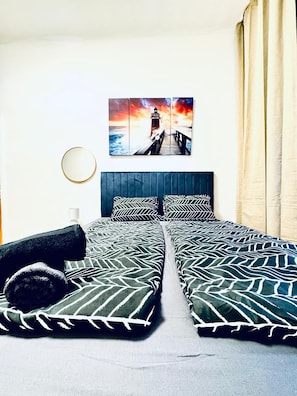 Un letto matrimoniale con biancheria decorata, una testiera, un quadro raffigurante un faro, uno specchio rotondo e una finestra con tende.