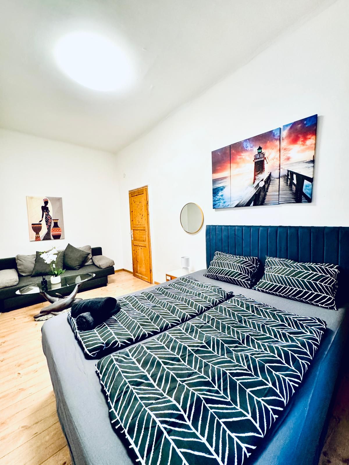 A modern bedroom with a bed, a sofa, and a painting of a lighthouse.