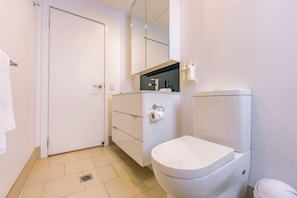 Een witte badkamer met toilet, wastafel en spiegel. Twee flessen handzeep hangen aan de muur.
