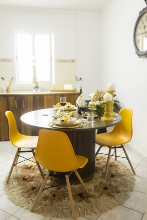 Un coin repas avec une table ronde, des chaises jaunes, un tapis moelleux et une horloge au mur.