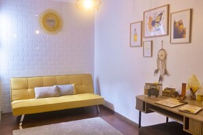 Um sofá amarelo, uma escrivaninha com uma máquina de escrever e obras de arte nas paredes, incluindo uma borboleta e um sol.