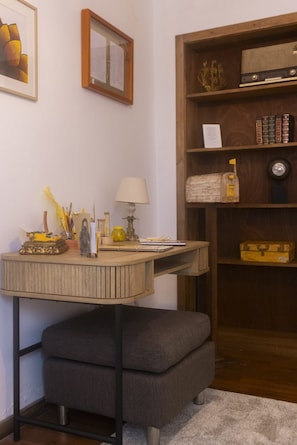 Une pièce comprenant un bureau, une lampe, une bibliothèque et un petit pouf.