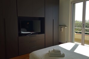 Un dormitori amb un llit, una televisió penjada a un moble i vista a un balcó amb barana.
