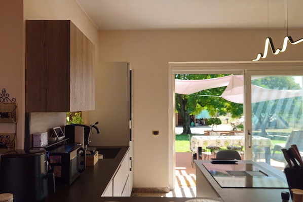 A modern kitchen with a built-in oven, a coffee machine, and a dining area with a table and chairs. - New Listing (Aprilia)