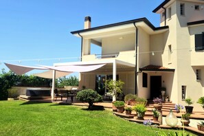 Una casa moderna amb una terrassa coberta, una zona de barbacoa i diverses plantes en testos.