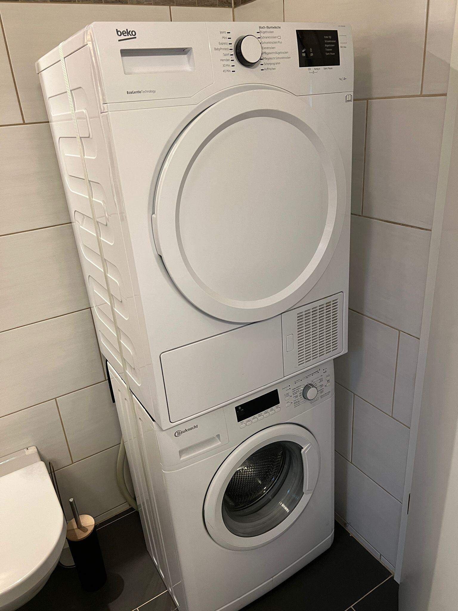 Una lavadora y secadora apiladas en un baño con baldosas blancas.