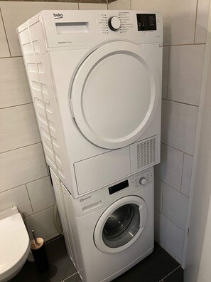 Máquina de lavar e secar empilhadas num banheiro com azulejos brancos.