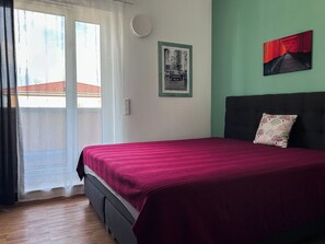 Quarto com cama, janela com cortinas, luminária na parede e quadro emoldurado.