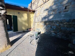 A courtyard with a metal chair, a table, and a ladder against a stone wall. - New Listing (Sanremo)
