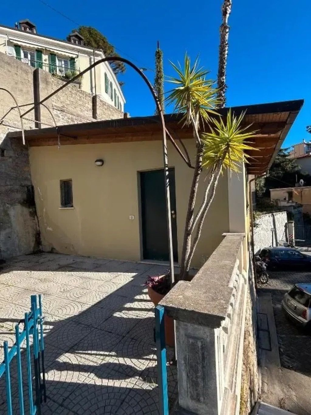 A building with a small door, a paved courtyard, and a blue fence.