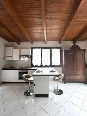 A modern kitchen with white cabinets, a central island, two bar stools, and a wooden ceiling. - New Listing (Sanremo)