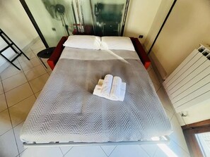 A bed with a patterned bedspread, two rolled towels, and a red bench beside it. - New Listing (Sanremo)