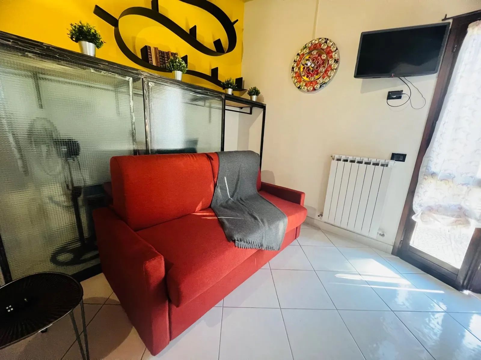 A red sofa with a grey throw, a TV mounted on the wall, and a radiator.