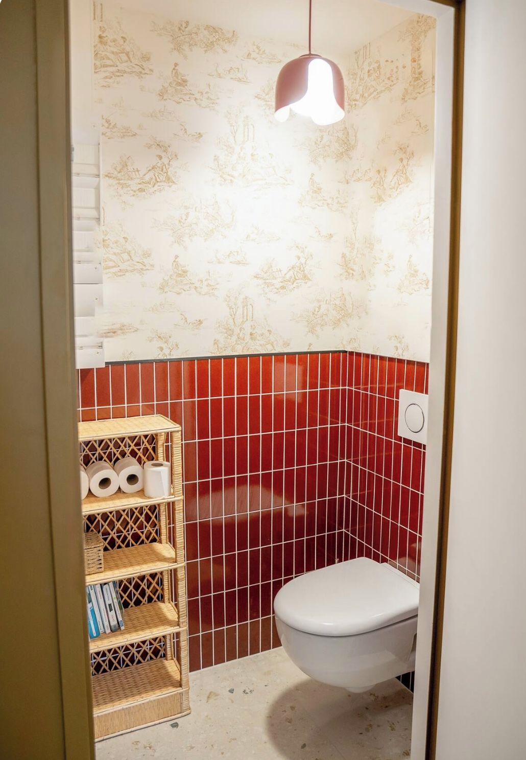 Un baño con inodoro, estante con artículos de aseo y pared estampada.