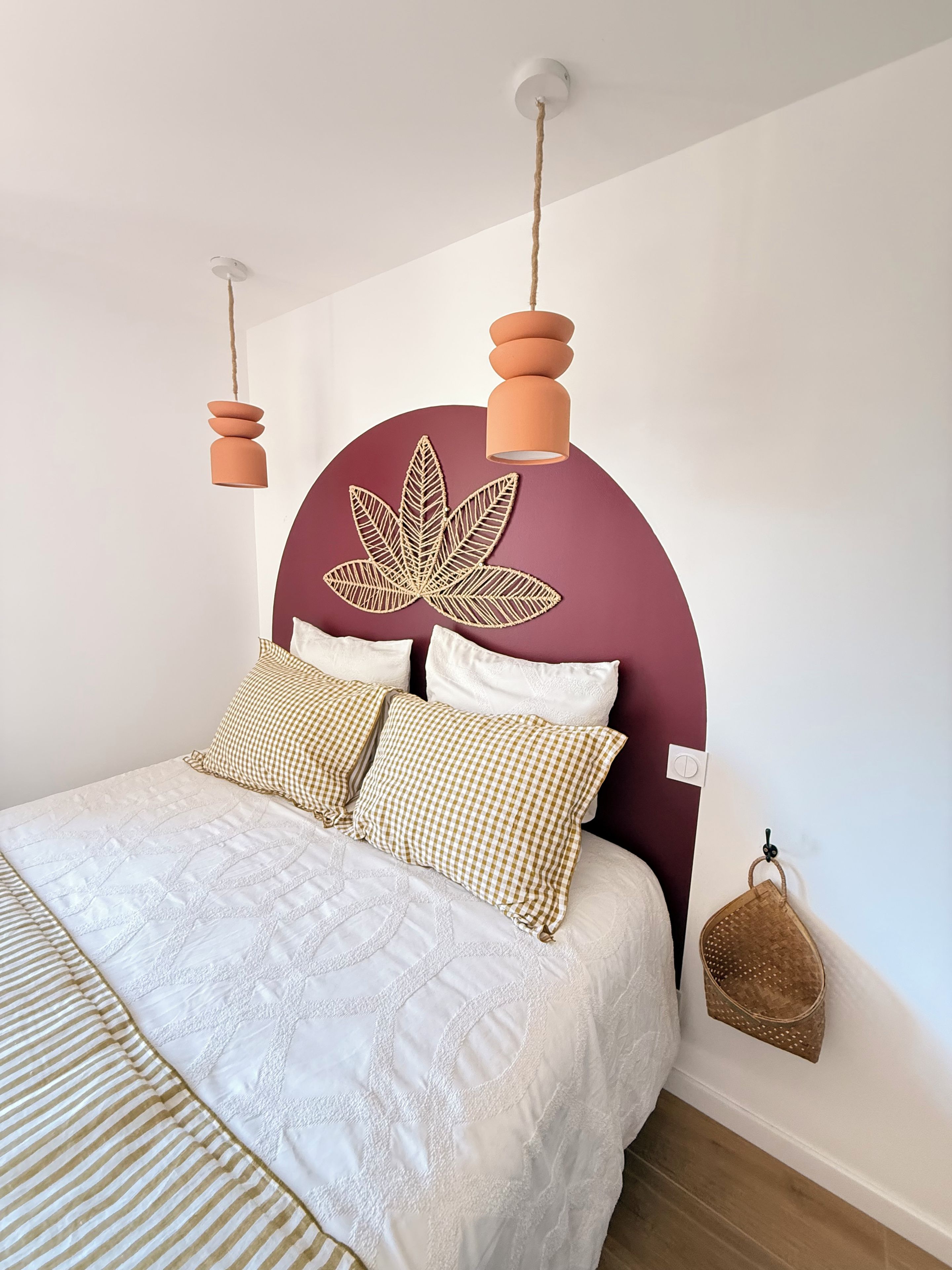 Una cama con colcha blanca acolchada, dos almohadas a cuadros y un cabecero con diseño de hojas.