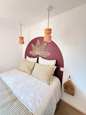Una cama con colcha blanca acolchada, dos almohadas a cuadros y un cabecero con diseño de hojas.