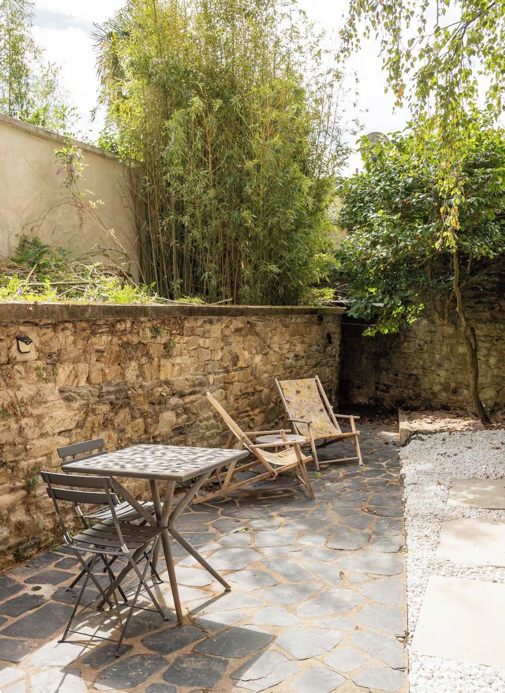 Un patio exterior con suelo de piedra, dos mesas de metal y sillas de madera.