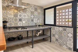 Una cocina con estufa a gas, un lavamanos y un ventanal con celosía decorativa.