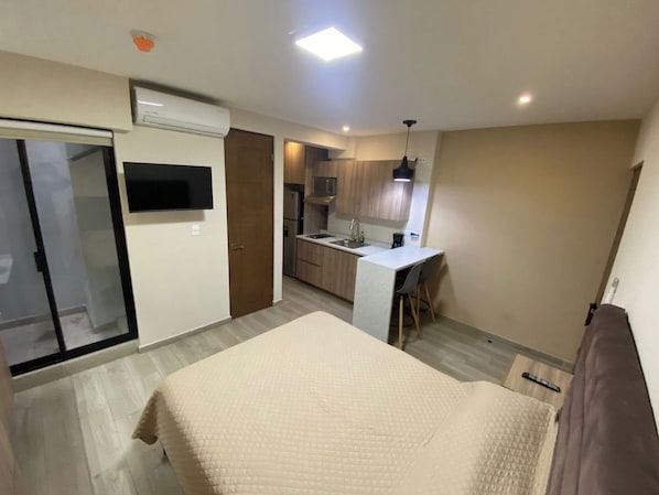 Ein Schlafzimmer mit einem Bett, einem Fernseher und einer kleinen Küche im Hintergrund.