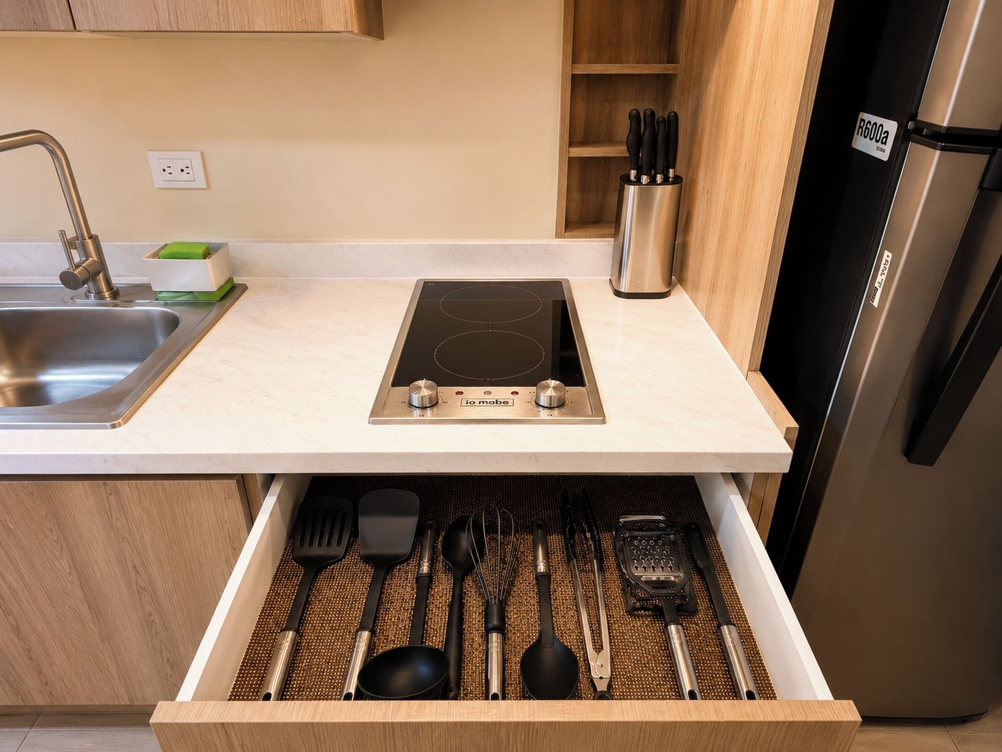 A kitchen with a stainless steel sink, a built-in induction cooktop, and a drawer organizer with utensils.