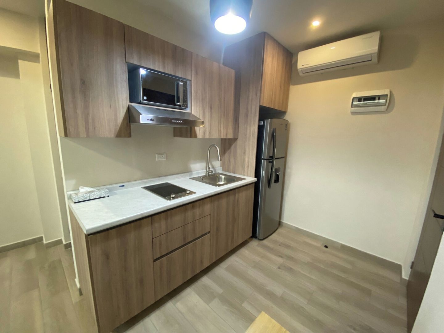 A modern kitchen with wooden cabinets, a stainless steel refrigerator, a microwave, and a built-in oven.