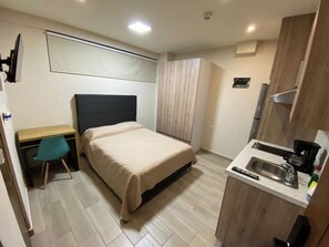 A compact hotel room with a bed, a desk, a chair, a kitchenette, and a shower area. - Accommodations in a suite with a kitchenette. Smart TV and Air Conditioning | SB104 (San Nicolás de los Garza)