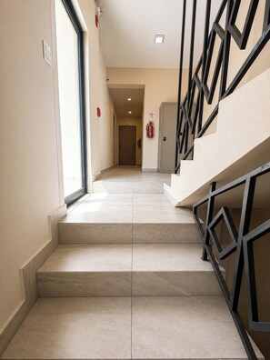 A staircase with a geometric railing design, a fire extinguisher mounted on the wall, and a door labeled '203' in the background. - Stay in San Nicolás. Queen-Size Bed | SB202 (San Nicolás de los Garza)