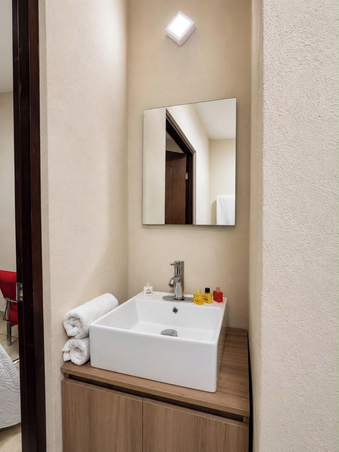 A bathroom with a white sink, a mirror, and toiletries on the countertop.
