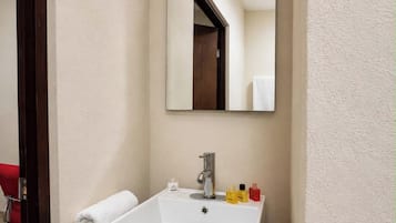 A bathroom with a white sink, a mirror, and toiletries on the countertop.