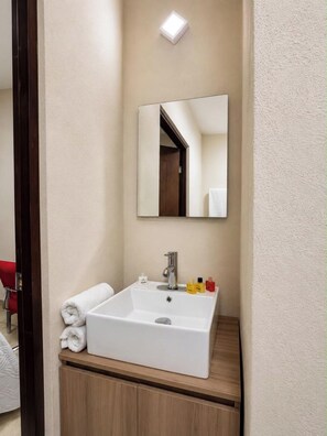 Une salle de bain avec un lavabo blanc, un miroir et des articles de toilette posés sur le comptoir.