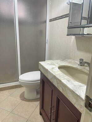Ein Badezimmer mit Toilette, einem Waschbecken mit Marmorplatte und einer Duschkabine.
