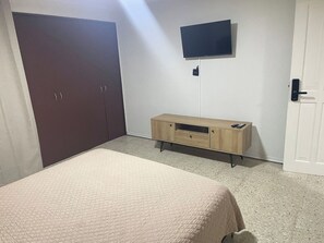 Ein Schlafzimmer mit einem Bett, einem Kleiderschrank, einem an der Wand befestigten Fernseher und einem Holzkabinett.