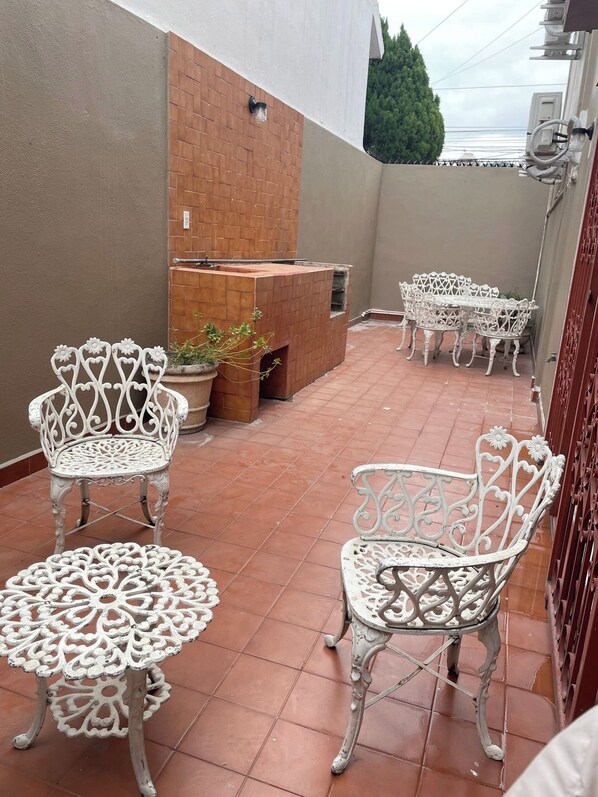 Eine Terrasse mit weißen schmiedeeisernen Stühlen und Tischen, einem Kamin aus Ziegeln und einem Fliesenboden.