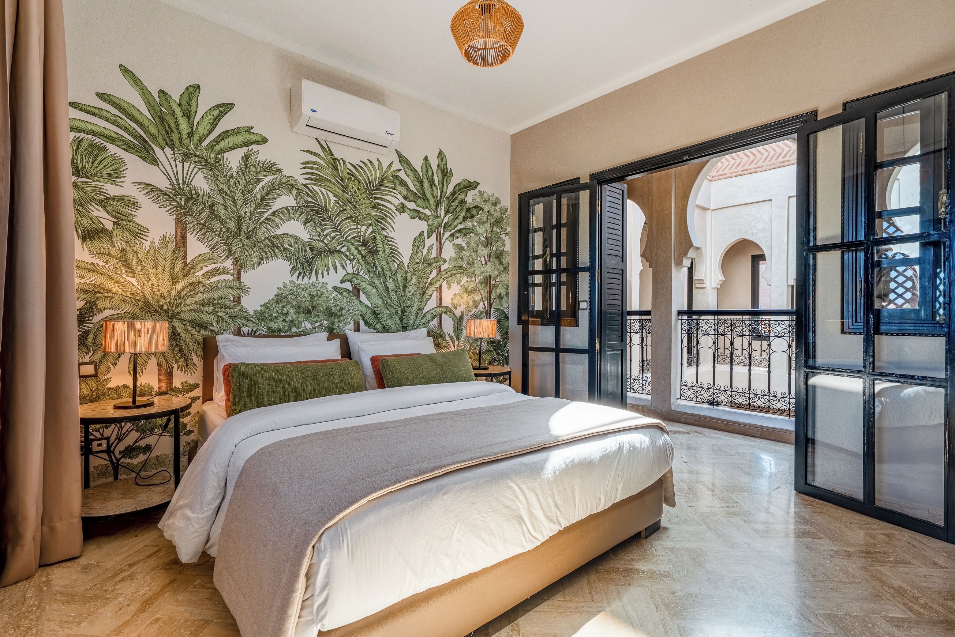 A bedroom with a bed, a nightstand, a lamp, and a large window with a view of an outdoor balcony.