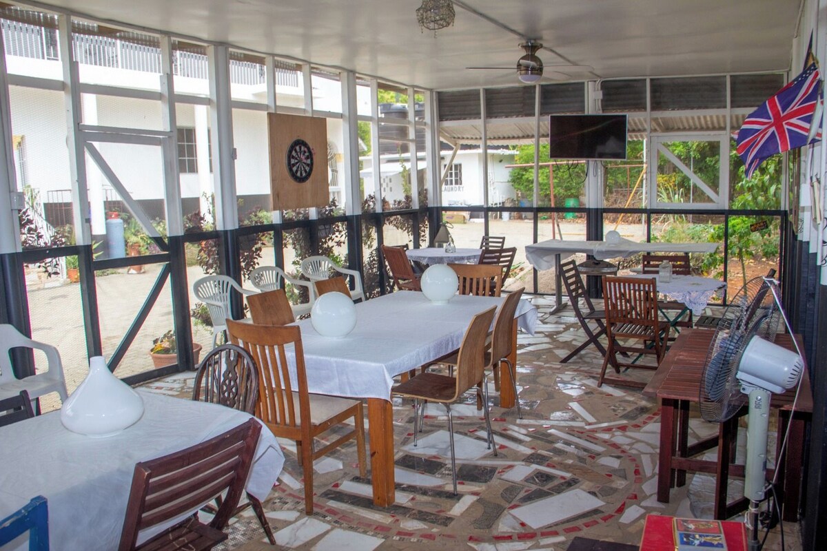 An outdoor dining area with tables and chairs, a dartboard, and a television screen.