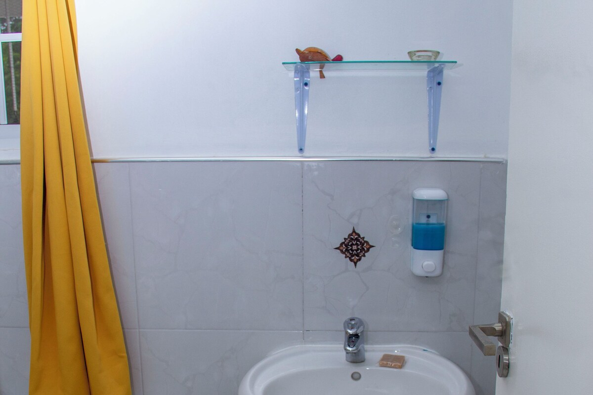 Un bany amb un lavabo blanc, una prestatgeria de vidre a sobre i una cortina de bany groga.