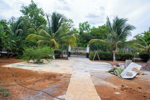 A gated entrance with a concrete pathway leading to a building, surrounded by palm trees and greenery. - Thebreeze2022 (St Toolies,  Tollgate, Clarendon Park)