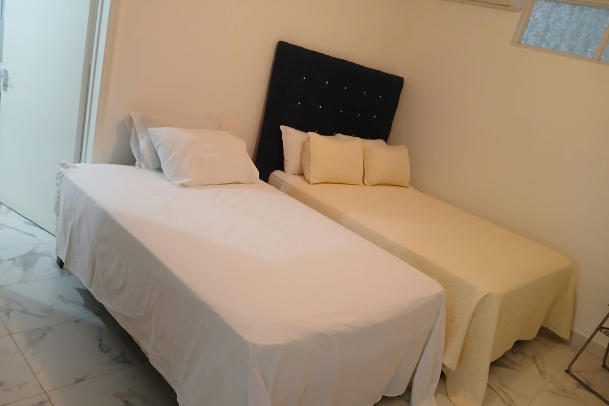 A room with two beds, one larger and one smaller, both with white bedding.