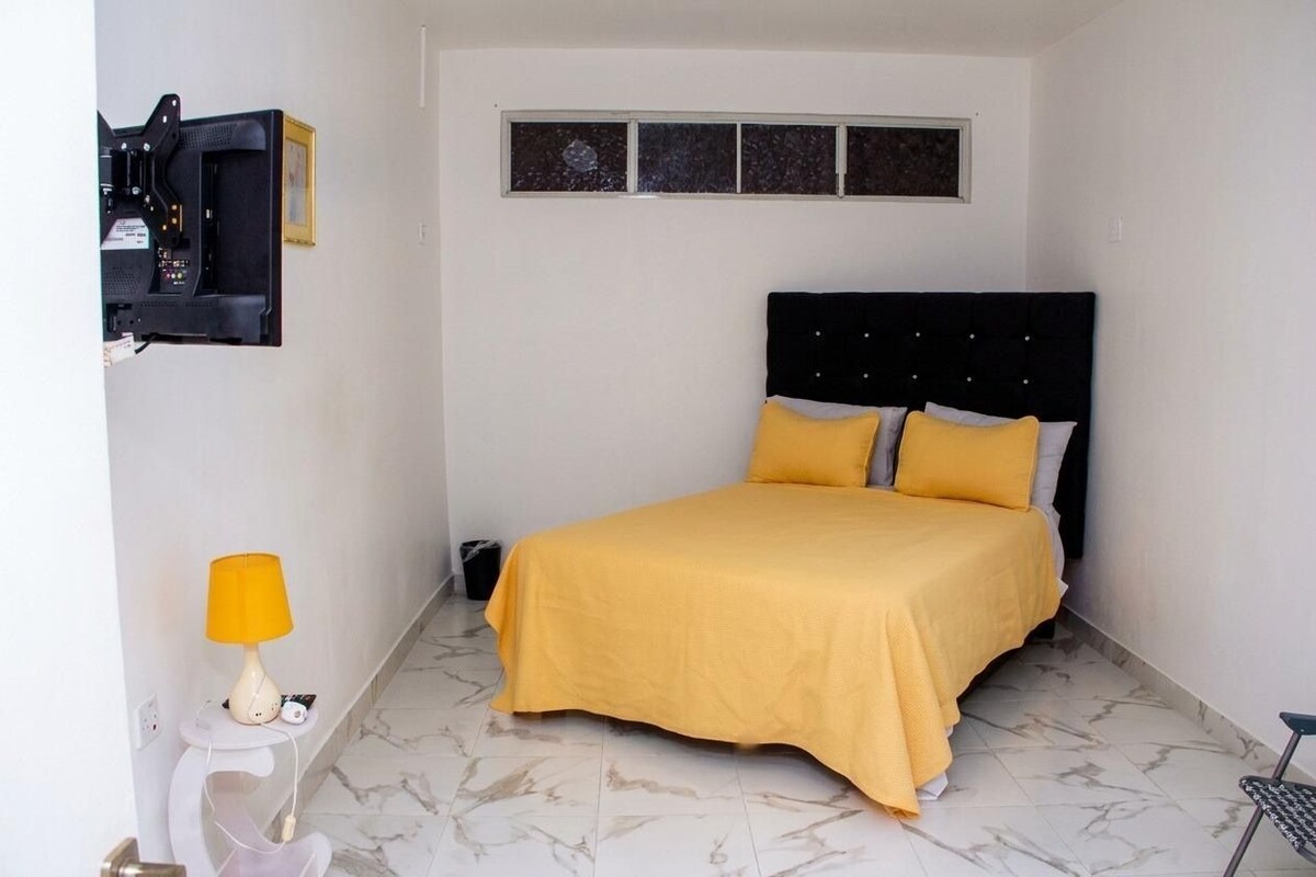 A bedroom with a bed, a television mounted on the wall, a lamp, and a small table.