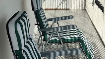 Une rangée de chaises longues avec des coussins à rayures, disposées sur un balcon dont le sol est orné de motifs.