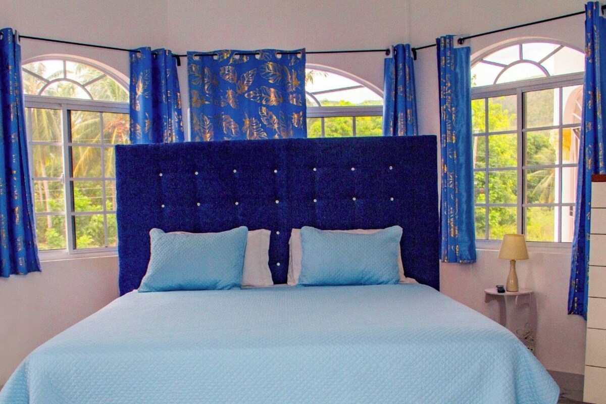 A bedroom with a bed, curtains, a television, a dresser, and a window.