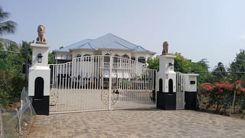 Une propriétéClose, avec un bâtiment blanc, deux statues de lions et un toit recouvert de tuiles bleues.