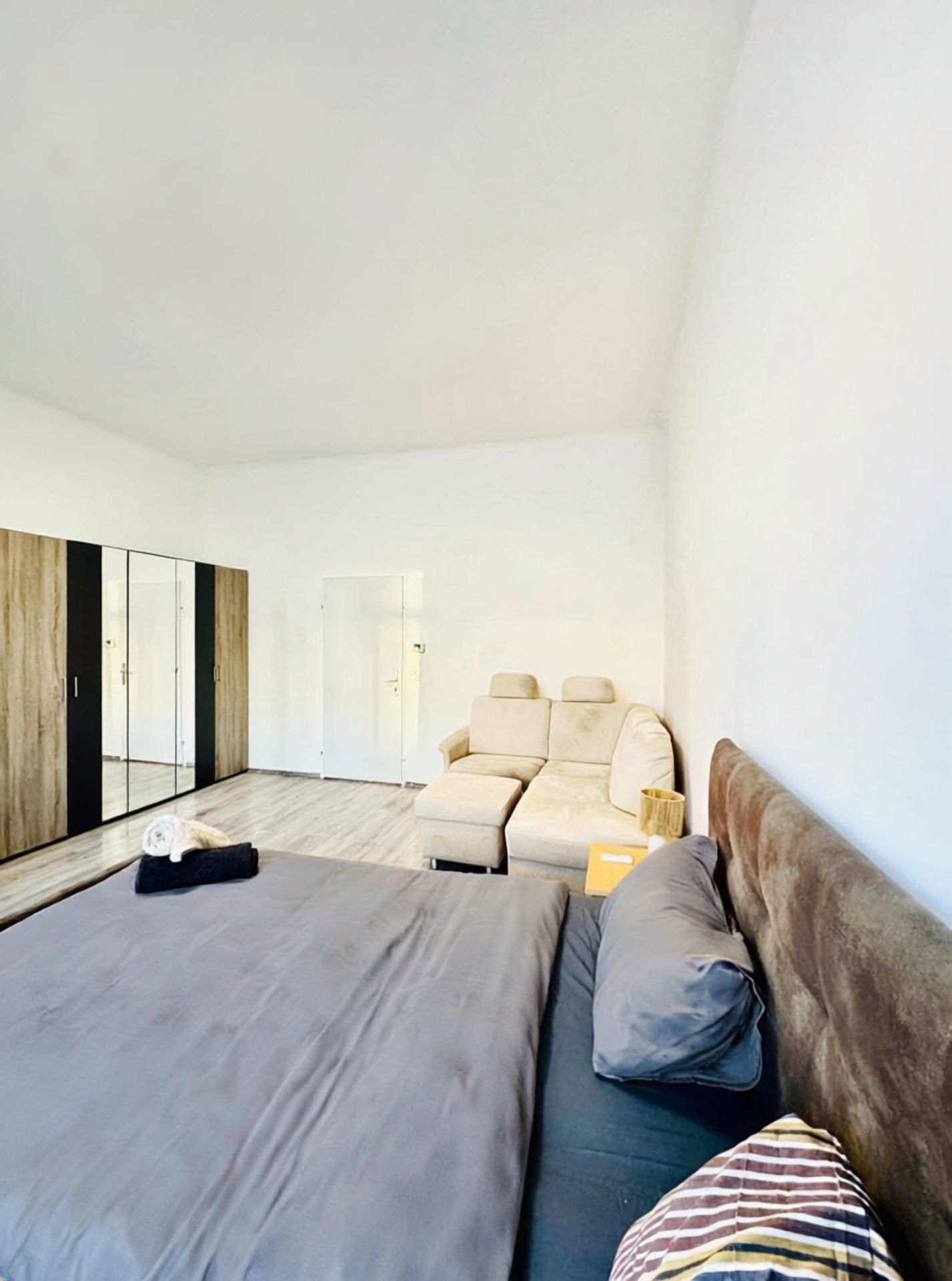 A bedroom with a bed, a sofa, a wardrobe, and a door.