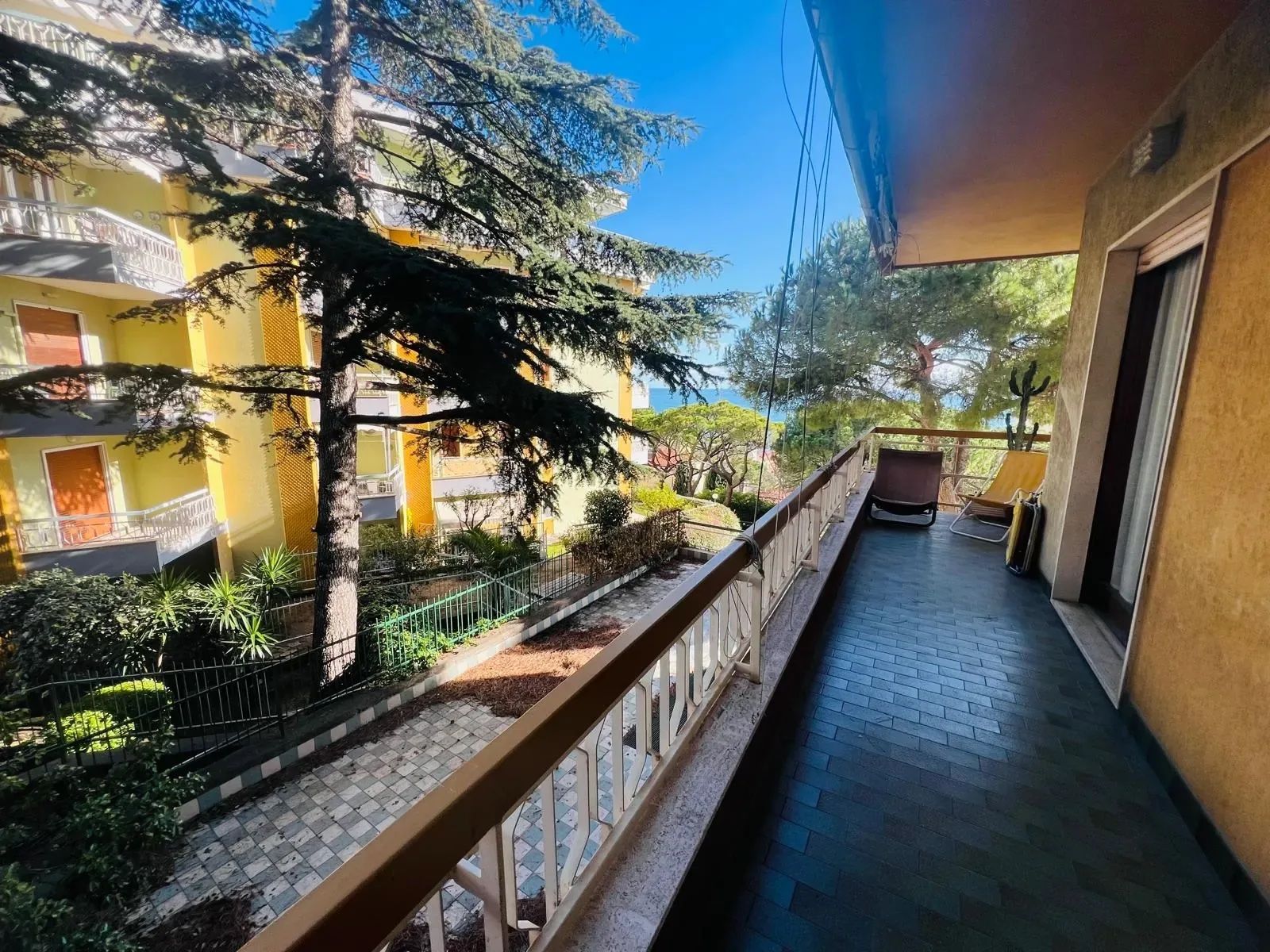 A balcony with a view of a building, a tree, and a chair.